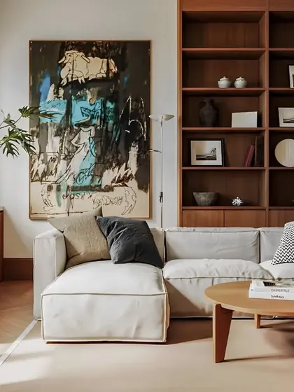 A comfortable and stylish living room with a large sectional sofa and a built-in wooden bookshelf. The abstract art and natural light make it a welcoming space.