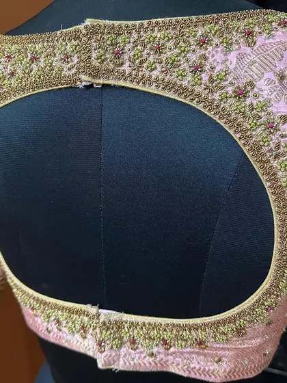 A close-up of an oval keyhole back on a light pink blouse. The entire opening is framed with incredibly detailed bead and thread work.