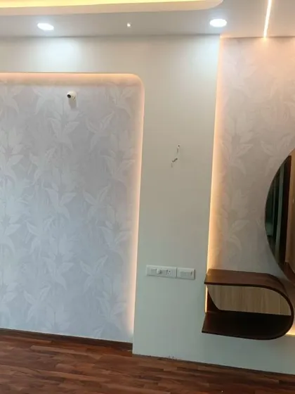 A modern bedroom featuring a subtle, light grey leaf pattern wallpaper. The design is integrated with custom lighting, creating a sophisticated and well-lit accent wall.