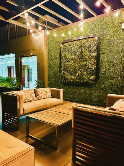 Another shot of the green wall lounge area, emphasizing the comfortable wooden furniture and the framed plant art on the wall.