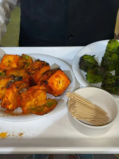 A server presenting freshly made Paneer Tikka and Hariyali Tikka, offering guests a choice of flavors.