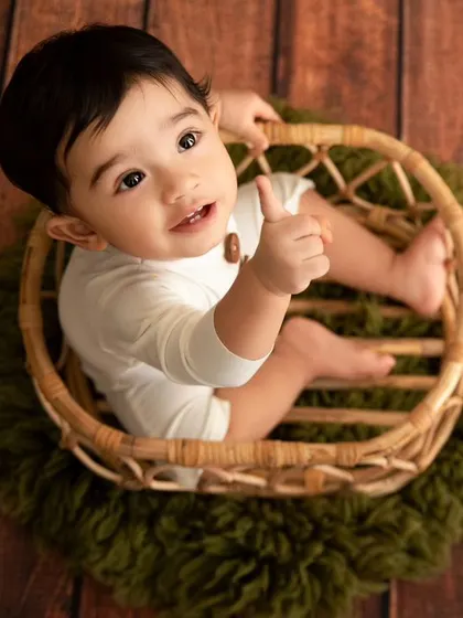 An overhead view of the baby boy in a wicker basket, pointing up during his fun jungle-themed shoot.