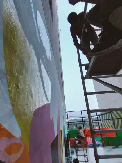 A view from the scaffolding, looking down at the evolving mural. The layers of color create a dynamic sense of movement.