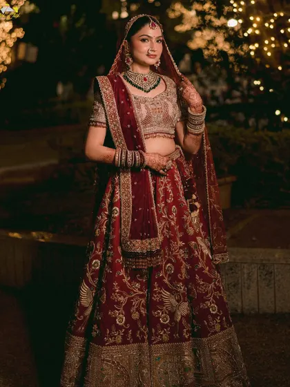 A full-length portrait of the bride in her rich, red lehenga. The warm lights of the trees create a magical bokeh effect, making her look like she's in a fairytale.