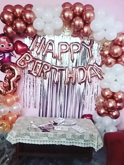 A cute Cocomelon-themed third birthday party at home. The setup includes a rose gold and white balloon arch over a silver shimmer curtain, perfect for a compact space.