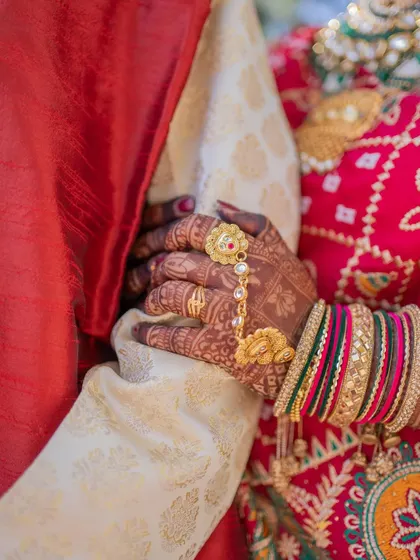 A close-up shot of the bride's hands, adorned with intricate mehndi and traditional jewelry, holding onto the groom's arm.