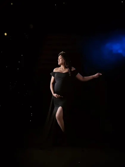 A dramatic and moody shot using creative lighting. The mom-to-be, in a classic black gown, is highlighted against a dark background, creating a powerful and artistic portrait.