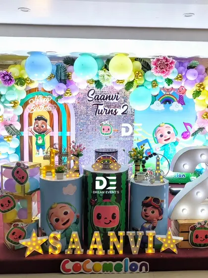 A colorful Cocomelon party for Saanvi's second birthday. The decor includes a large light-up number '2', a sequin backdrop, and lots of fun character details.