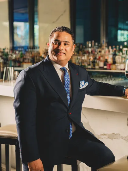 A classic portrait of a manager at Yauatcha, seated at the bar. The composition is designed to convey authority and sophistication, positioning him as a key figure in the restaurant's high-end service.