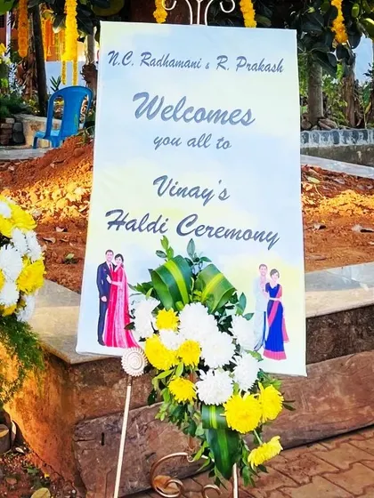 A wider shot of the haldi ceremony welcome sign, showing how it is positioned to greet guests as they arrive. The floral arrangement adds a touch of elegance to the simple sign.