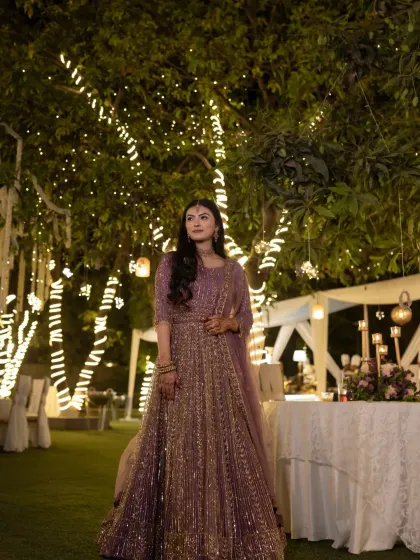 A bride standing under a canopy of fairy lights. This portrait captures the magical ambiance of an evening celebration and the elegance of her shimmering lavender lehenga.