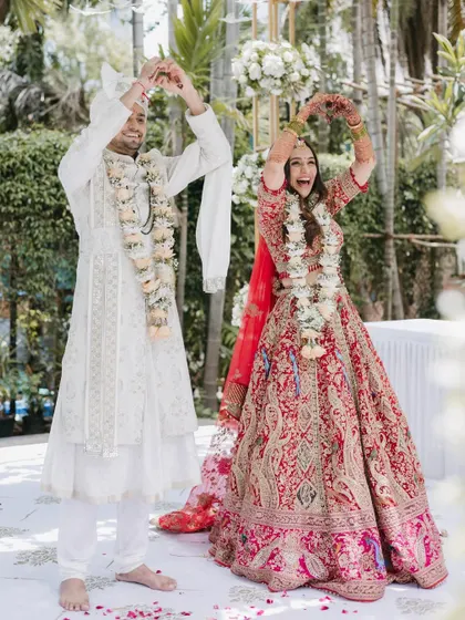 The couple shares a fun, choreographed pose during their ceremony, making hearts with their hands, reflecting their playful and happy personalities.