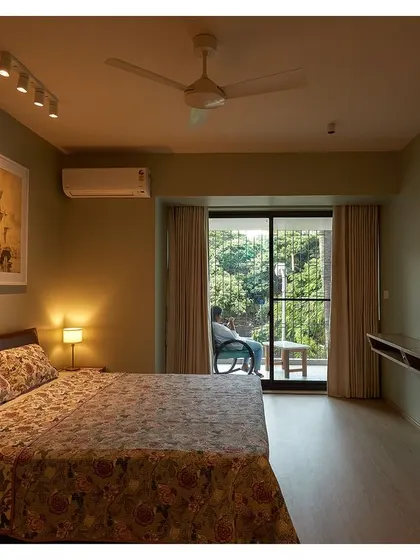 A bedroom with an olive green accent wall and a private balcony. The design connects the interior space with the greenery outside.