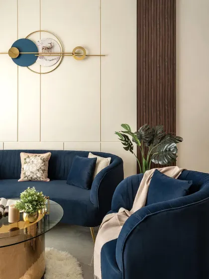 A detail shot focusing on the elegant curve of the blue sofa and the barrel-back accent chair. The modern wall art with gold and blue elements ties the entire composition together.