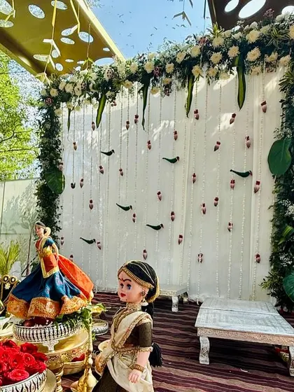 A traditional Varapooje backdrop with hanging floral strings and parrot motifs made of leaves, set against a clean white background.