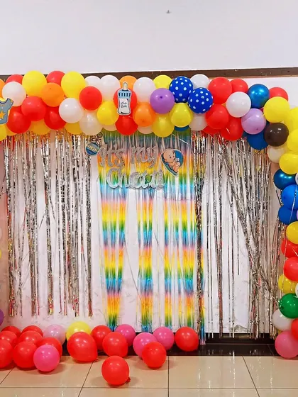 A full view of the "It's my Chatti" celebration decor. The colorful balloon arch and rainbow fringe curtain create a bright and cheerful backdrop for the family's special day.