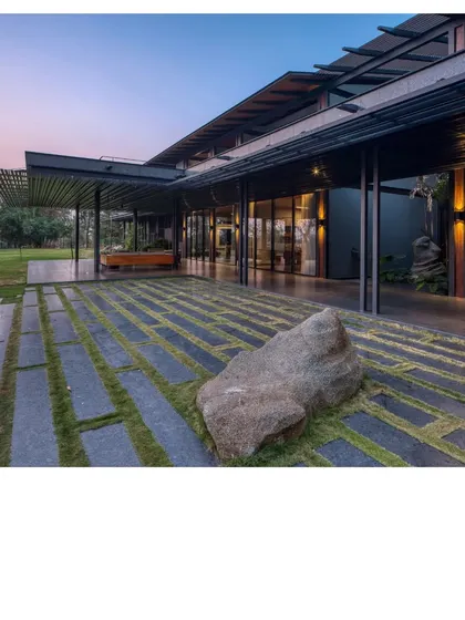 The verandah of the Lakeshore house, paved with stone slabs and interspersed with grass. A large, found rock sits as a natural sculpture, grounding the space and connecting it to the site's geology.