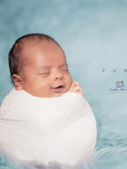 This is a classic 'potato sack' swaddle pose, which babies often find very comforting. The simple wrap and soft blue backdrop draw all the attention to the baby's sweet, sleepy smile.