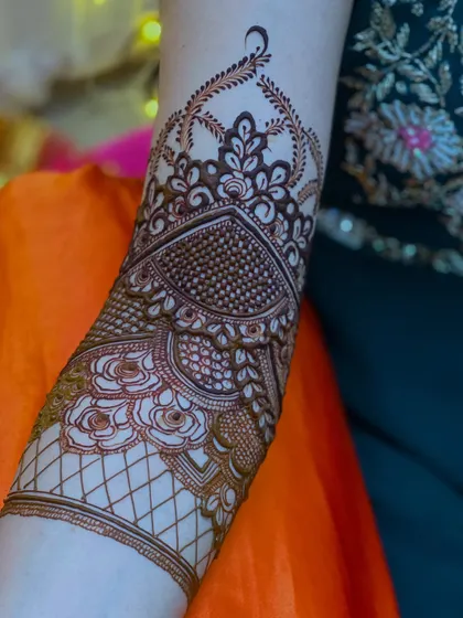 A close-up of a bridal arm piece. This design features a beautiful heart-shaped pattern filled with delicate dot work, a popular element in modern bridal henna.
