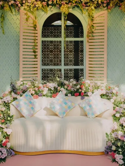 A beautiful photo-op spot with a sofa nestled within an explosion of pastel flowers, set against a mint-green window frame. This creates a perfect, Instagrammable moment for the couple and guests.