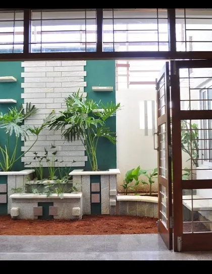 Viewed from the interior, the courtyard at the Prabhakar Residence becomes a living mural. The wide, foldable wooden doors allow the space to be fully opened up, merging the indoor living area with the outdoor garden.