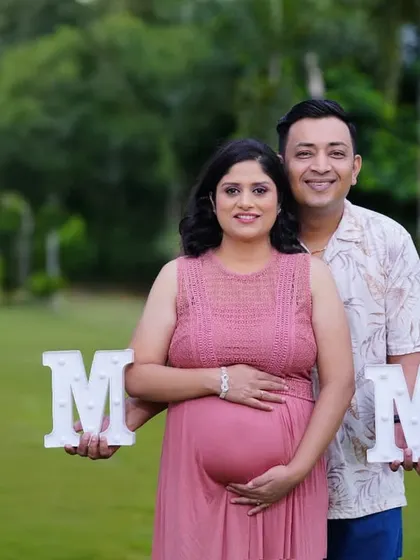 A happy couple holding "MOM" props during their outdoor maternity session. Using props in a natural setting adds a fun and personalized touch to the photos.