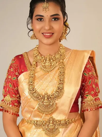 A smiling bride in a silk saree wearing a complete antique-finish temple jewellery set. This includes the choker, long necklace, and waist belt.
