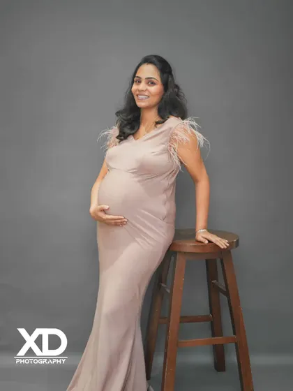 A simple and elegant solo maternity portrait against a clean grey studio background.