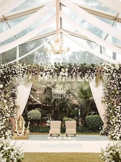 A grand wedding stage inside a clear-span tent. The decor is lush with white flowers and greenery, creating an elegant and classic look.