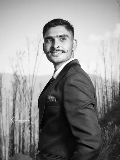A handsome groom in a stylish suit, captured in a timeless black and white photo. The natural, outdoor setting with trees in the background adds a rustic charm.