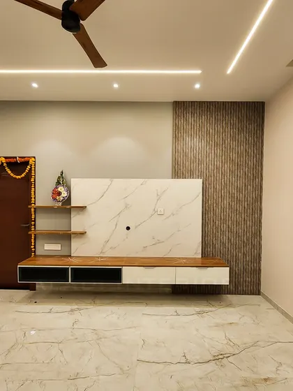 A contemporary living room TV unit with a white marble backdrop and fluted wood paneling. The floating console and open shelves provide a clean, uncluttered look.