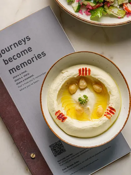 A bowl of creamy hummus next to a menu. This shot combines the food with the restaurant's branding, creating a cohesive image for social media or press features.
