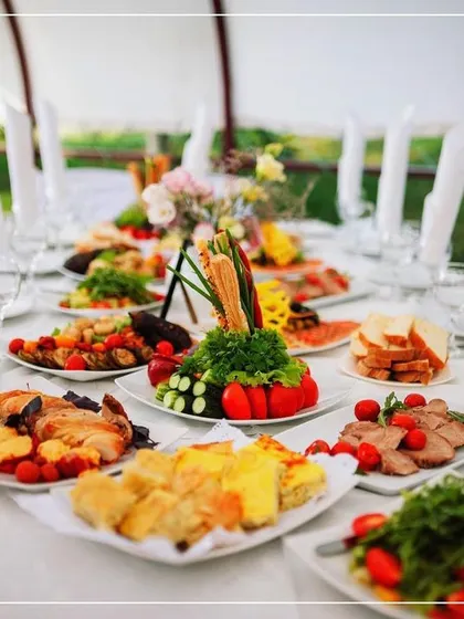 A beautifully set table for an outdoor event. Each place is set, and the center of the table is filled with family-style platters, showcasing a more communal and interactive dining format.