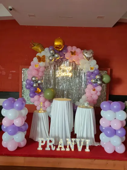 A pastel balloon ring in purple, pink, and white with a silver tinsel curtain.