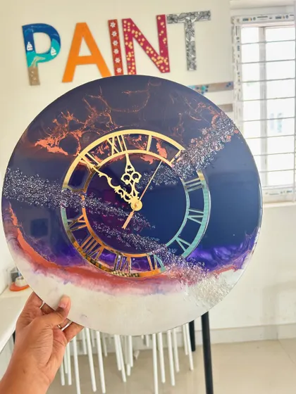 A galaxy-inspired resin clock with deep blues, purples, and sparkling glitter, held up in our studio.