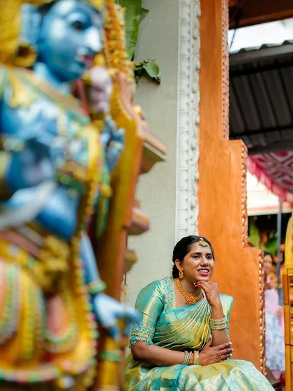 A vibrant portrait of a bride framed by colorful temple statues, highlighting the rich cultural setting of her engagement.