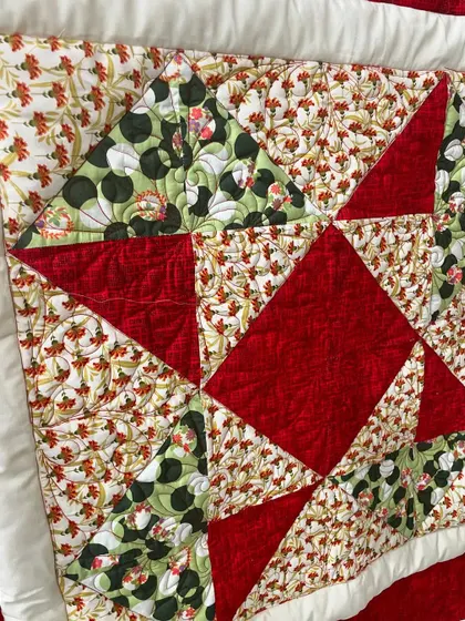 A close-up of the red and green baby quilt, showing the mix of floral and solid fabrics.
