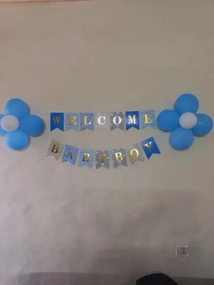A simple and sweet "Welcome Baby Boy" decoration. This setup includes a blue and gold banner flanked by two blue and white balloon flowers, perfect for a low-key home celebration.