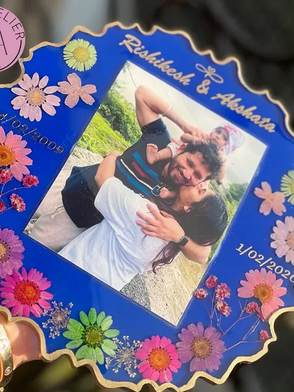 A vibrant blue resin frame celebrating a family's journey. It features a happy family photo along with two important dates, bordered by a rainbow of colorful preserved flowers.