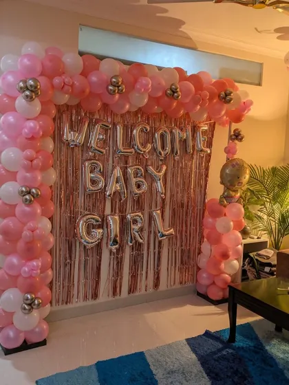 A view of the pink and white 'Welcome Baby Girl' balloon arch under warm indoor lighting, creating a cozy and celebratory atmosphere.