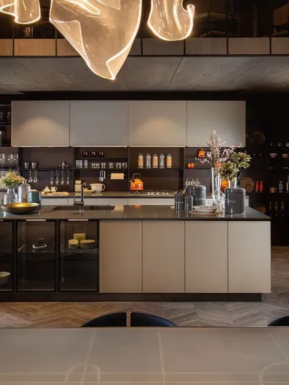 Our kitchen designs are engineered for high utility without compromising on aesthetics. This open-plan kitchen features an expansive island with an integrated glass crockery unit, ample backsplash storage, and a seamless blend of neutral tones and dark accents.