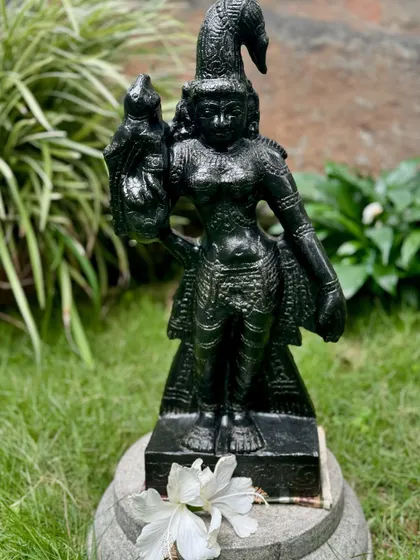 Our Madurai Meenakshi statue, hand-carved from black granite, stands gracefully in a garden, her form inspired by the art of Tamil Nadu.