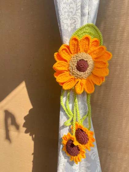 A close-up of the sunflower curtain tie in action. The bright yellow flower and dangling smaller sunflowers create a lovely, cascading effect.