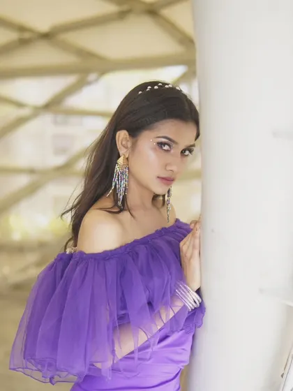 A close-up portrait showing the off-shoulder ruffled neckline of the purple gown. It's a stylish and contemporary design.