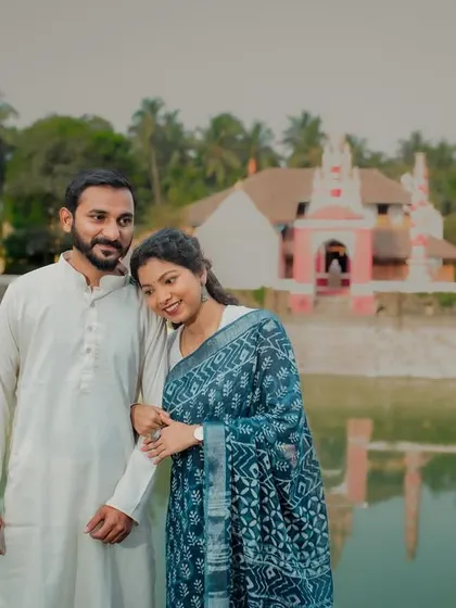 A happy portrait of the couple in front of a traditional temple. The bride leans on her partner's arm, both smiling, capturing a moment of shared faith and love.