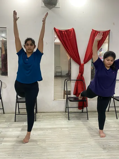 Practicing a standing balance pose with the support of a chair, making it accessible for all fitness levels.