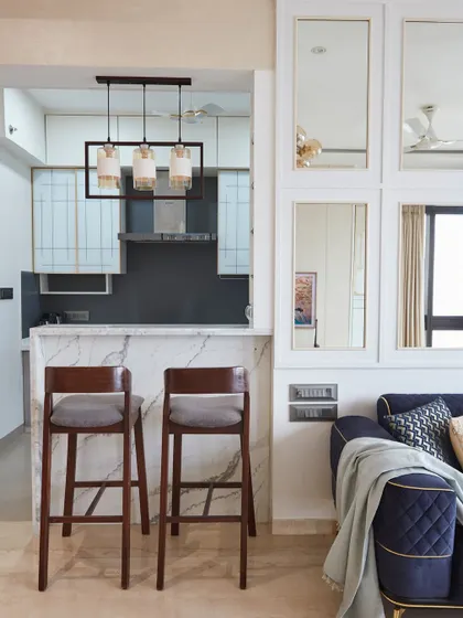 The open layout of this living room flows seamlessly into a modern kitchen, complete with a sleek marble breakfast counter and bar stools. The design is perfect for social and connected living.