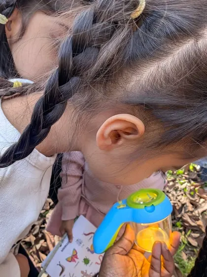 Two girls peer into a bug viewer, their braids mirroring their shared focus and curiosity. These walks are wonderful for making new friends who also love nature.