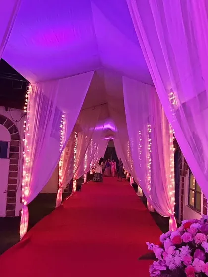 A dramatic entrance tunnel created with draped fabric and vibrant purple and pink lighting. The red carpet adds a touch of classic glamour to this striking entryway.