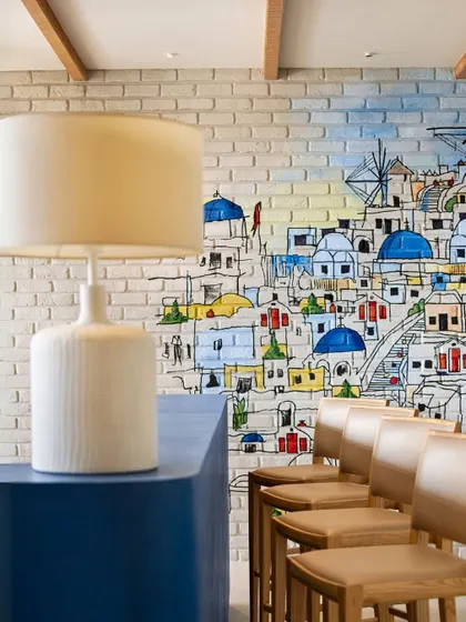 A vibrant mural of a coastal town on a brick wall, adding a touch of artistry and escapism to a bar area.